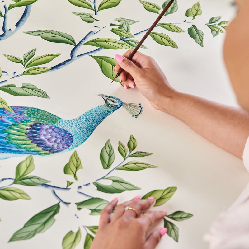 Diane Hill painting a chinoiserie style peacock and climbing tree onto silk wallpaper