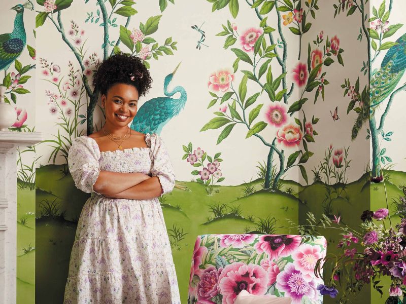 Diane Hill standing in front of her 'Florence' chinoiserie wallpaper made in collaboration with Harlequin