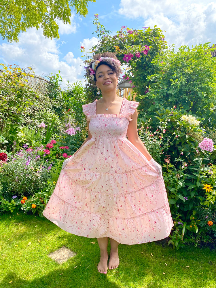 Diane Hill models the nap dress created by Hill House Home in collaboration with Phenomenal and Netflix, featuring her bespoke pink chinoiserie design, standing in a garden
