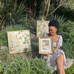 Diane Hill showcasing 3 framed botanical gold leaf paintings from 'Garden of Secrets' collection in garden