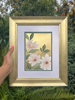 hand holding framed botanical chinoiserie painting on gold leaf paper featuring a three pink and white flowers