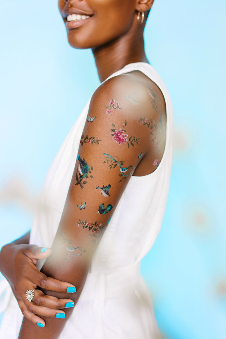 A smiling woman shows off her arm, bearing Chinoiserie inspired temporary tattoos, design by Diane Hill in collaboration with Tattly