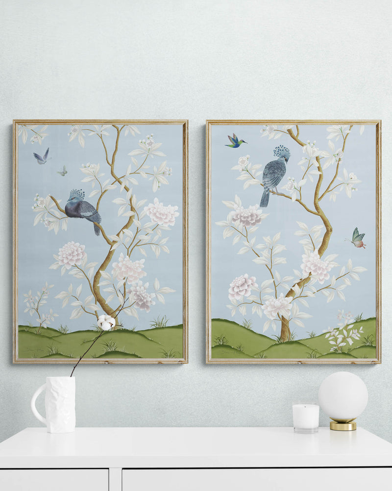 2 framed blue chinoiserie wall art prints with botanical illustrations featuring birds, butterflies, and flowers hung on wall