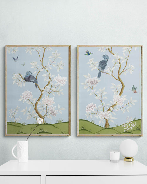 pair of 2 framed blue chinoiserie wall art prints with botanical illustrations featuring birds, butterflies, and flowers hung on wall