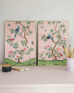 pair of 2 framed pink and green chinoiserie wall art prints with botanical illustrations featuring birds, butterflies, and flowers hung on wall