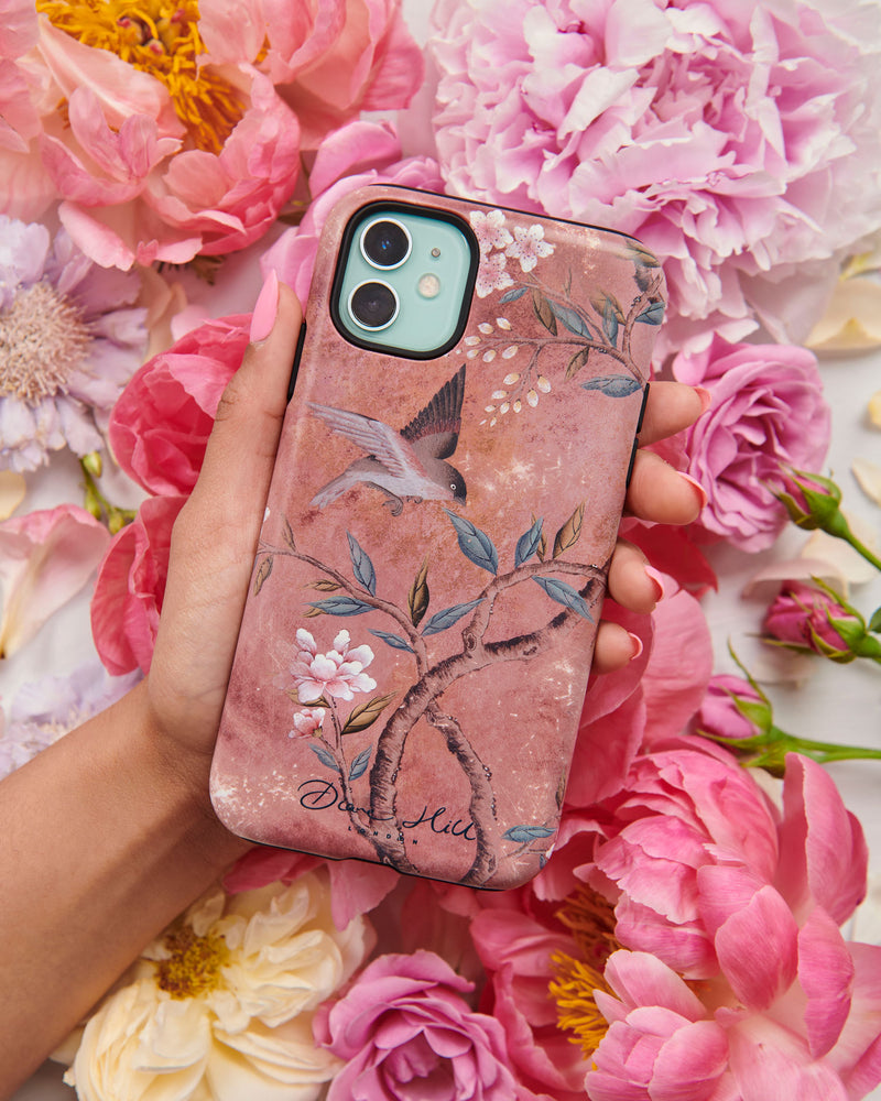 Hand holding luxury chinoiserie phone case featuring vintage inspired bird branches and flowers on a distressed mottled background