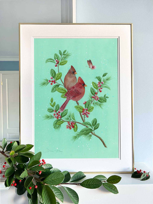 framed winter-themed chinoiserie art print featuring two cardinals and butterfly on a holly branch on green snowy background