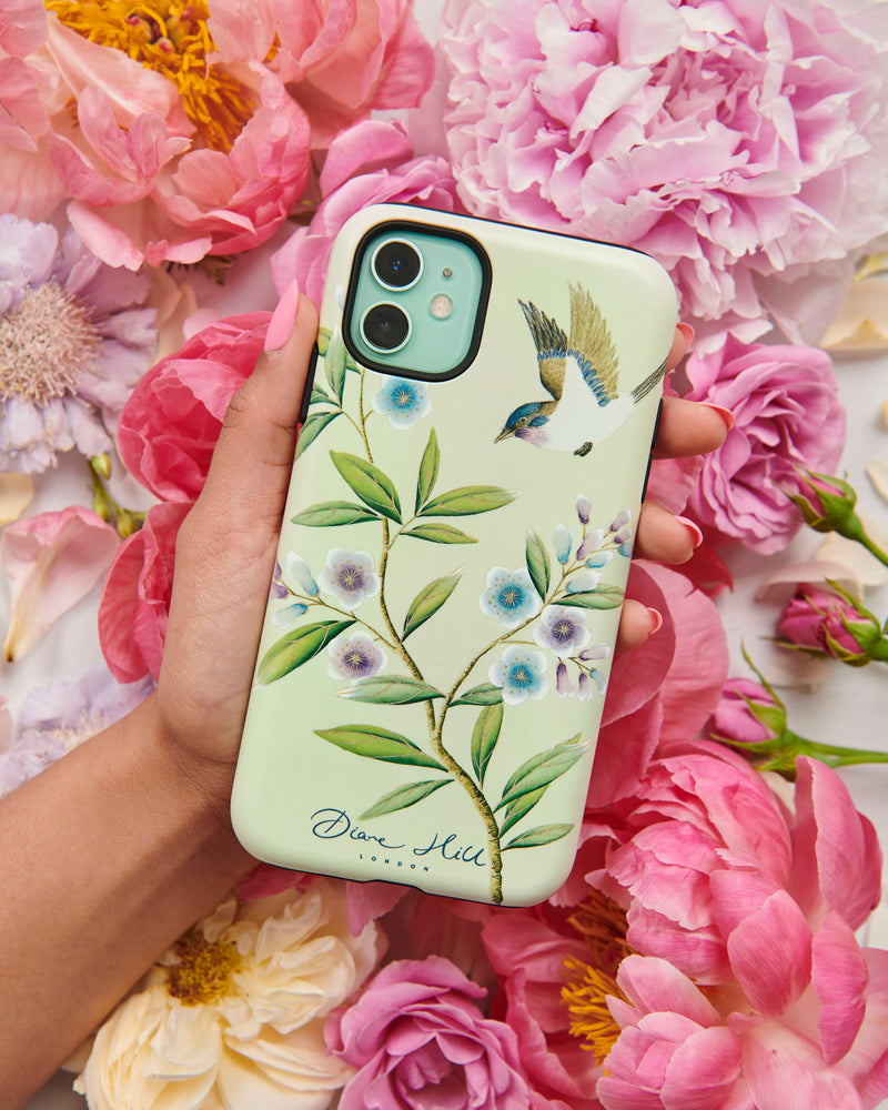 Hand holding luxury chinoiserie phone case featuring vintage inspired bird branches and flowers on a green background
