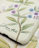 close up of luxury chinoiserie phone case featuring vintage inspired bird branches and flowers on a green background
