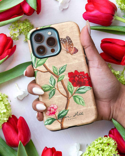 Hand holding luxury chinoiserie phone case featuring vintage inspired butterfly branches and flowers on a gold background
