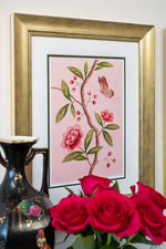 framed chinoiserie wall art print featuring pink vintage-style butterfly and flower branch on pink background hung on wall