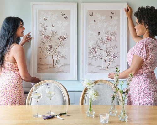 pair of two soft pink framed chinoiserie wall art prints featuring butterflies, flower branches, and bamboo hung on wall