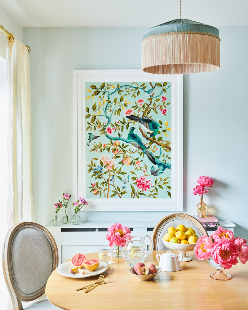 framed blue modern chinoiserie wall art print featuring two birds, flowers, branches, and fruit on blue background hung on wall