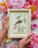 two hands holding framed botanical mini art print of yellow exotic bird on branch with flowers and leaves
