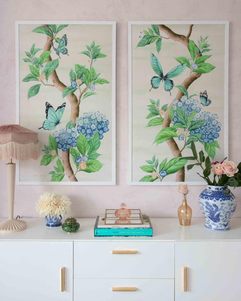pair of two framed Chinoiserie style art prints featuring butterflies and blue flowers on an ivory cream background hung on wall