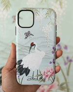 hand holding luxury chinoiserie phone case featuring Japanese inspired crane, flowers, and wisteria on a blue mountain background