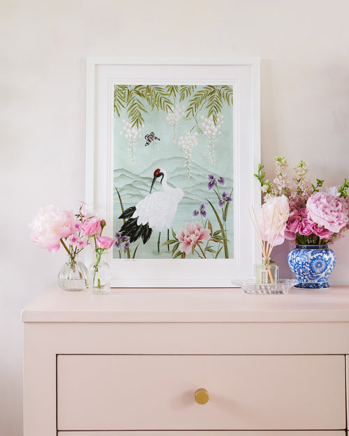 framed chinoiserie wall art print featuring Japanese inspired crane, flowers, and wisteria on a blue mountain background on bedside table