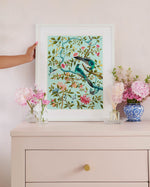 framed blue modern chinoiserie wall art print featuring two birds, flowers, branches, and fruit on blue background on set of drawers