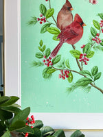 close up of framed winter-themed chinoiserie art print featuring two cardinals and butterfly on a holly branch on green snowy background