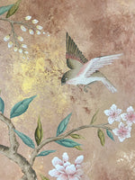 close up of framed vintage style chinoiserie painting featuring a bird and blossom branch on a distress mottled bronze and gold background