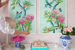 close up of a pair of two framed Chinoiserie style art prints featuring butterflies and pink flowers on an aqua blue background hung on wall