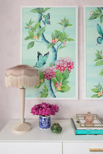 close up of a pair of two framed Chinoiserie style art prints featuring butterflies and pink flowers on an aqua blue background hung on wall