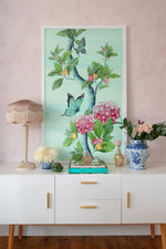 framed Chinoiserie style art print featuring butterflies and pink flowers on an aqua blue background hung on wall