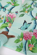 hand holding Chinoiserie style art prints featuring butterflies and pink flowers on an aqua blue background