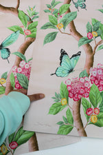 hand holding pair of Chinoiserie style art prints featuring butterflies and pink flowers on a pastel pink background 