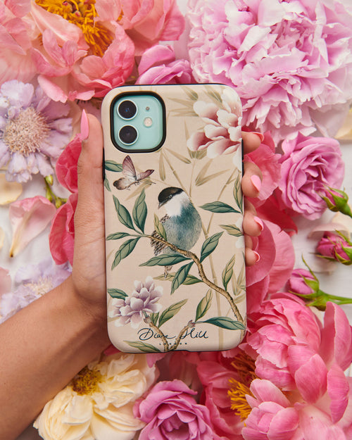 hand holding pink luxury phone case featuring vintage style bird, butterfly and flower branches with a bamboo background