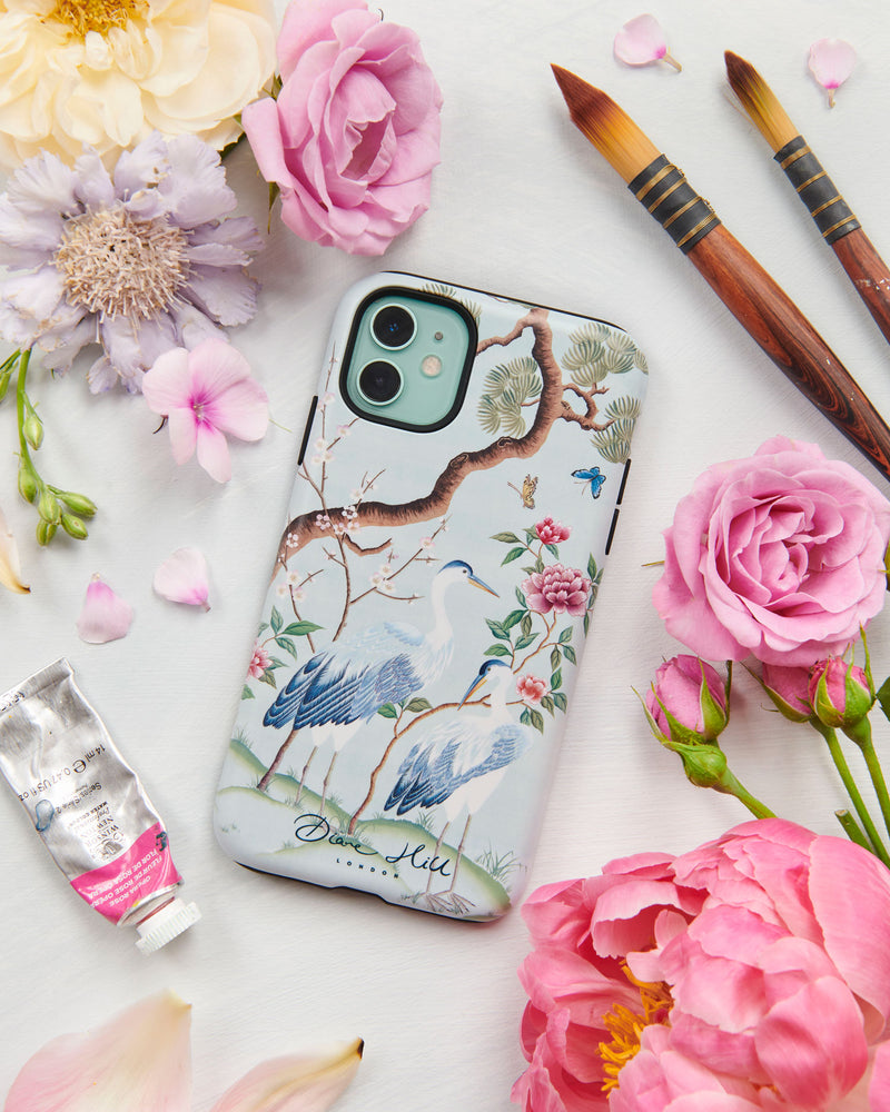 blue luxury chinoiserie phone case featuring antique inspired herons, flowers, and blossoms beneath a pine tree with butterflies