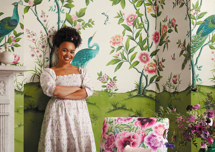Diane Hill standing in front of botanical chinoiserie wallpaper mural designed in collaboration with Harlequin
