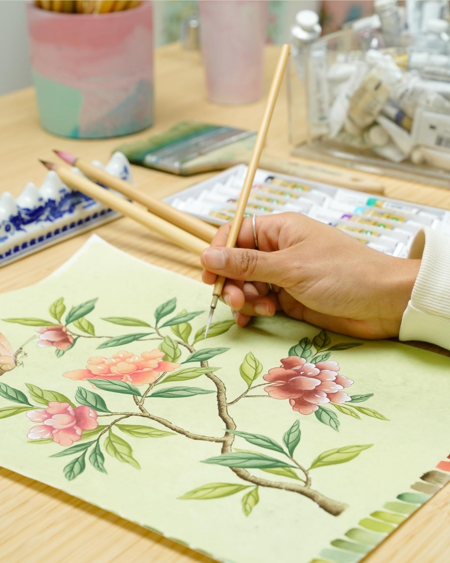 hand holding Chinese paintbrush painting chinoiserie style flowers and branches on silk painting paper