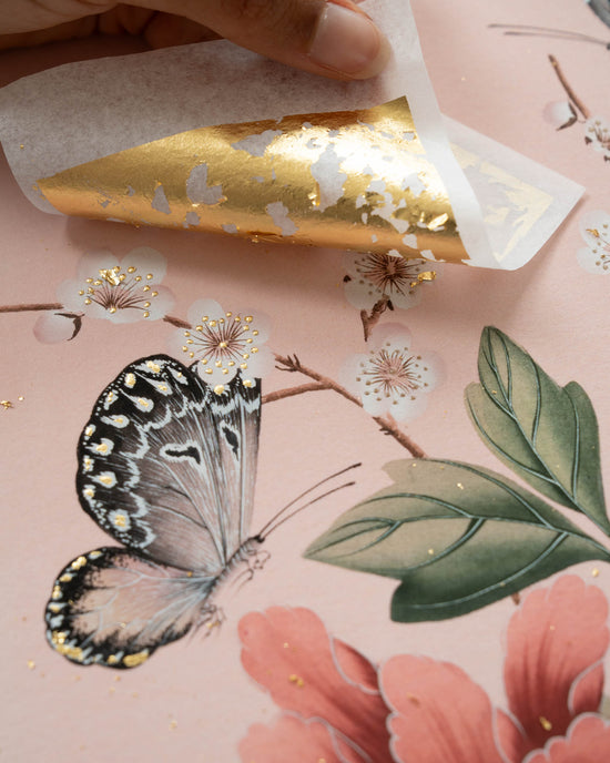 24 carat goldleaf being applied to pink chinoiserie art print featuring red flowers, cherry blossoms, and butterflies