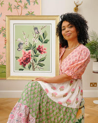 chinoiserie artist diane hill holding framed botanical wall art prints featuring japanese cherry blossoms, butterflies, and flowers