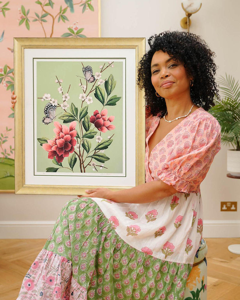 chinoiserie artist diane hill holding framed botanical wall art prints featuring japanese cherry blossoms, butterflies, and flowers