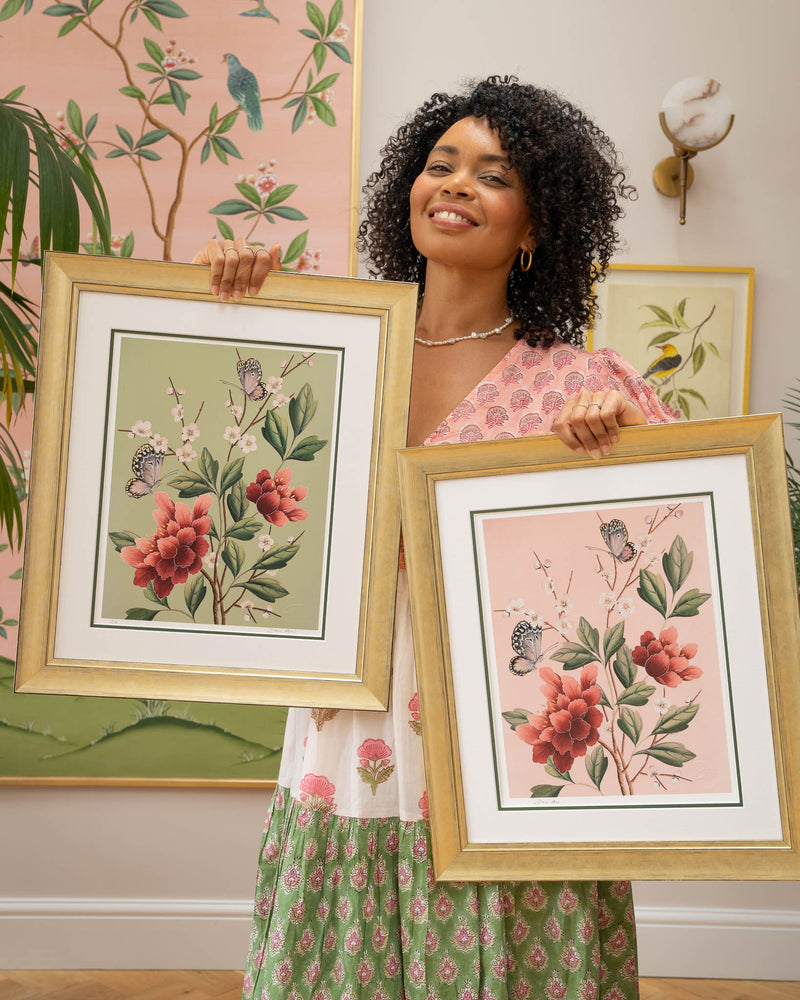 chinoiserie artist diane hill holding two framed botanical wall art prints featuring japanese cherry blossoms, butterflies, and flowers 