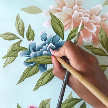 Diane Hill's hands holding a paintbrush, painting on the details of a chinoiserie flower in one of her floral paintings