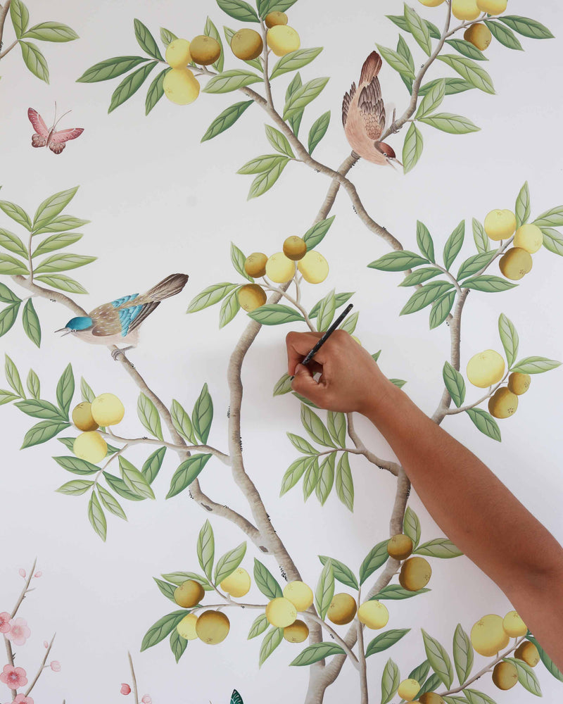 Diane Hill painting the chinoiserie wallpaper design she created for Rebel Walls. Featuring branches and yellow plums on a tree with a bird perched on a branch