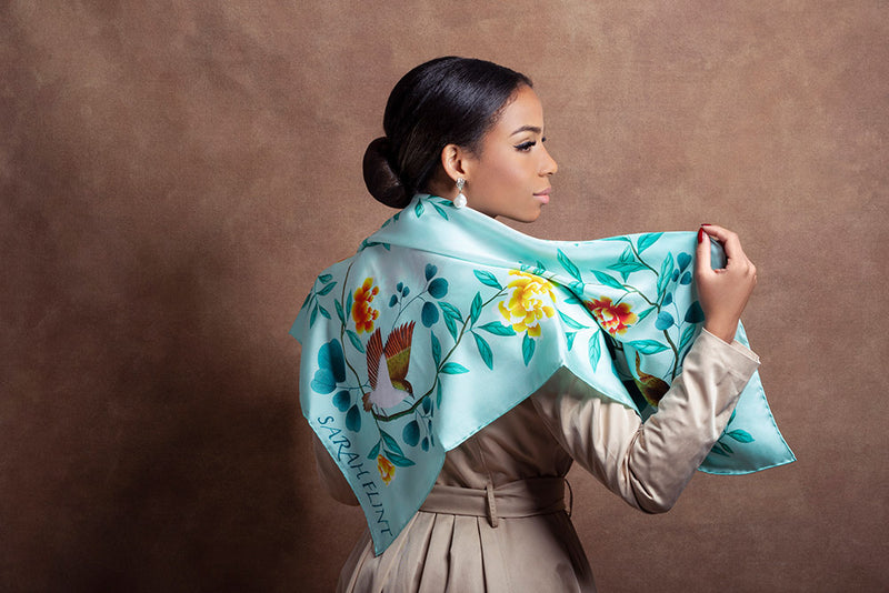 A model wears a silk scarf by Sarah Flint, featuring a turquoise botanical design featuring peonies and birds by Diane Hill