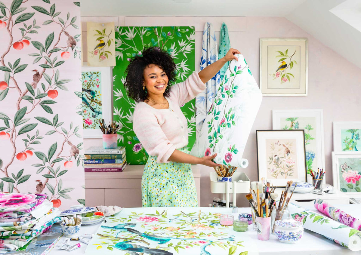 Diane Hill in her studio holding up a roll of her chinoiserie wallpaper