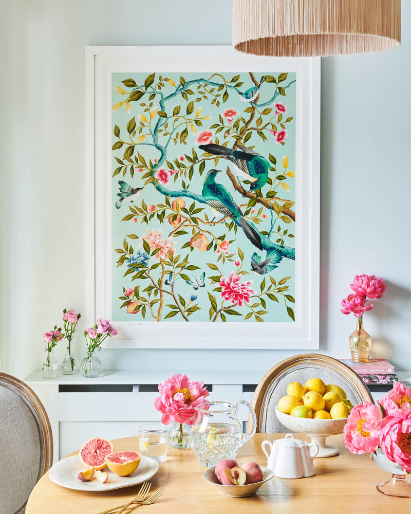 framed blue modern chinoiserie wall art print featuring two birds, flowers, branches, and fruit on blue background hung on wall