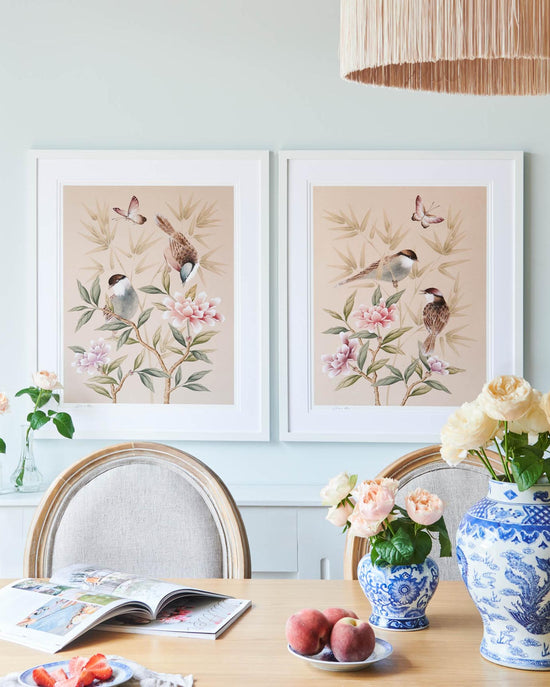 set of two blush pink framed chinoiserie wall art prints featuring vintage style birds, butterfly and flower branches with a bamboo background hung on wall