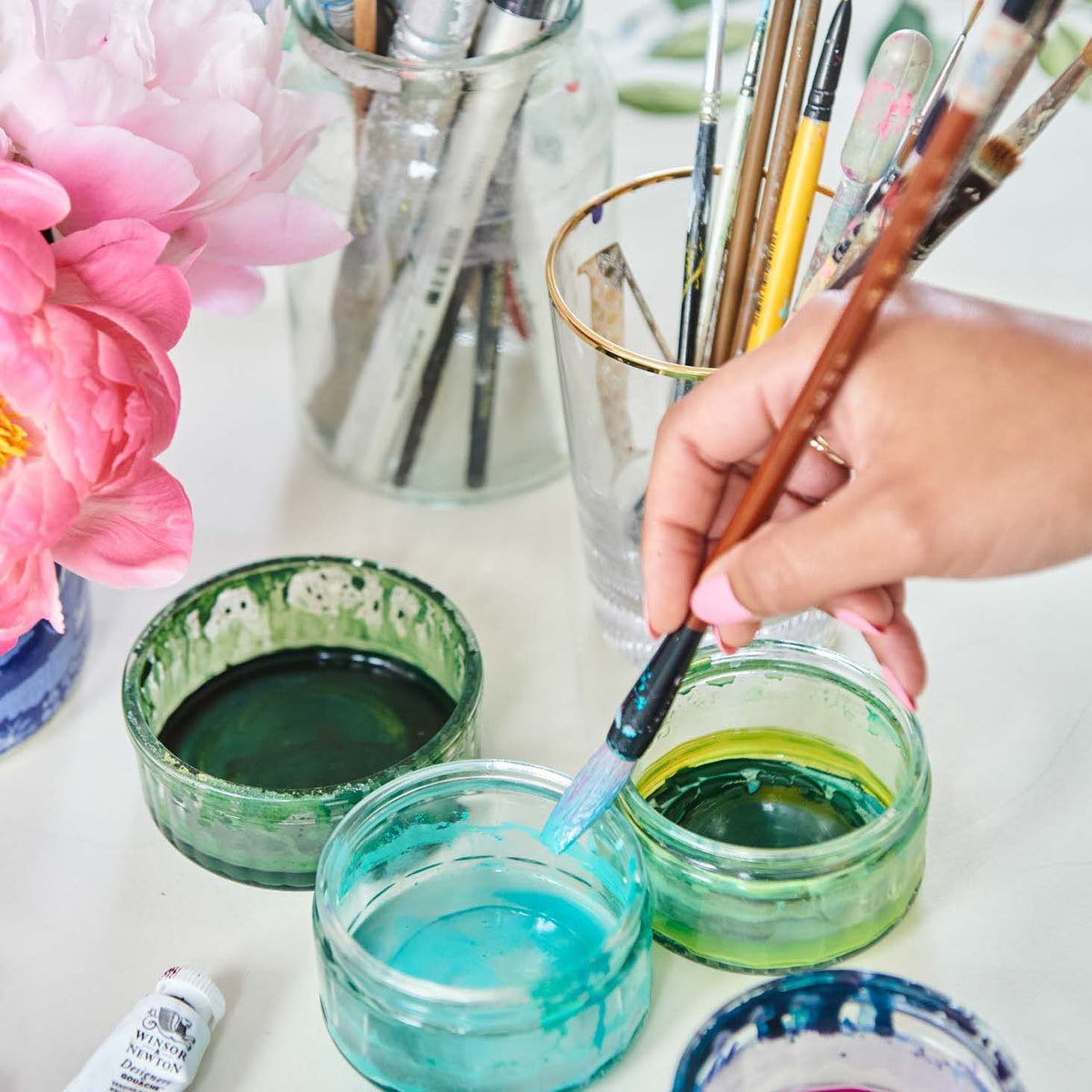 Diane Hill dipping a paintbrush into a small ramekin of blue paint