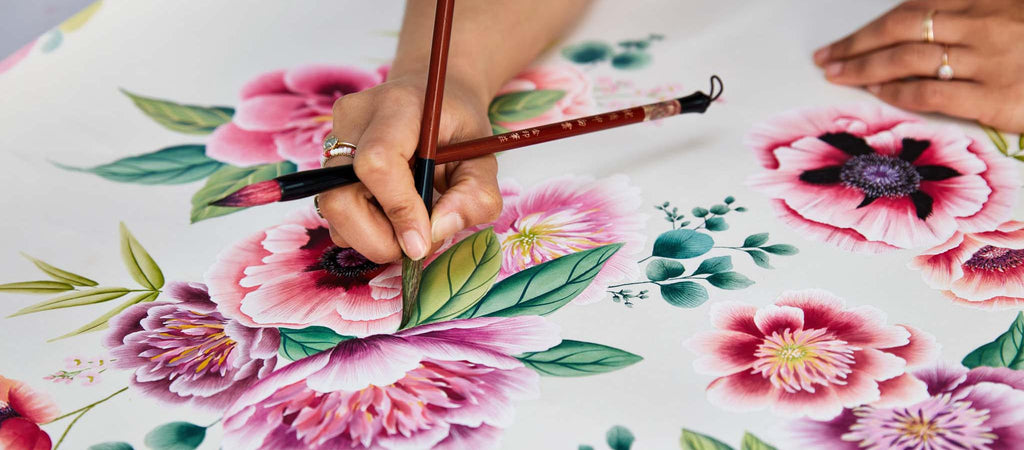 Up close photo of Diane Hill painting the details of a chinoiserie flower as part of her wallpaper design on silk paper