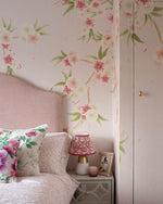 Pink and white floral cherry blossom wallpaper mural in pink bedroom wshowing the headboard and bedside. Wallpaper over door to create a jib door effect