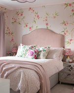 Girls bedroom pink flower blossom mural wallpaper in pink bedroom with double bed and pink headboard with floral pillows and bedspread. Flower blossom design cascades down from the ceiling with a soft pink background