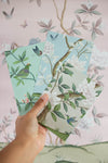 hand holding 3 chinoiserie mini wall art prints in multi colours featuring botanical illustrations of birds, flowers, butterflies, and trees