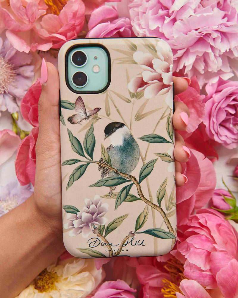 hand holding pink luxury phone case featuring vintage style bird, butterfly and flower branches with a bamboo background