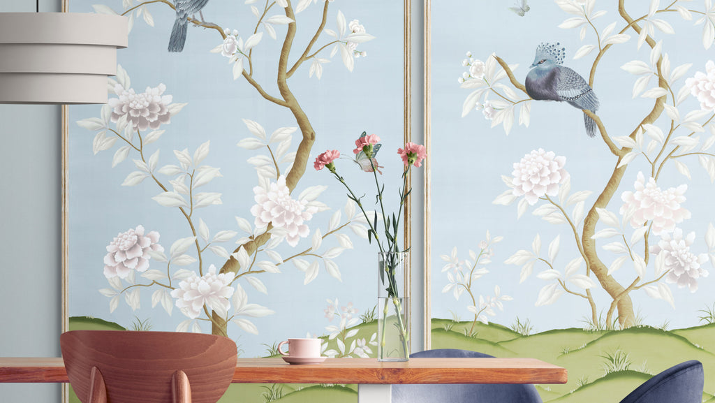 two blue framed chinoiserie wall panel prints mounted on a wall behind a modern looking wooden dining table and chairs